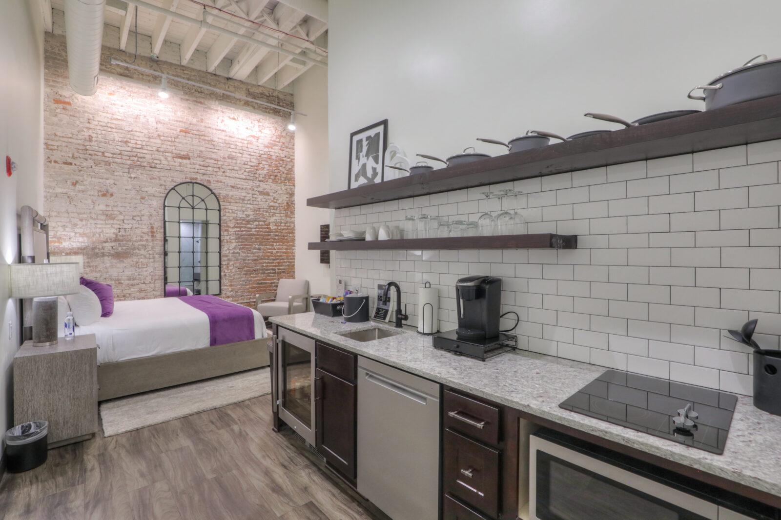 A wide view of a hotel suite with a kitchenette, sitting area, and bed in the background.